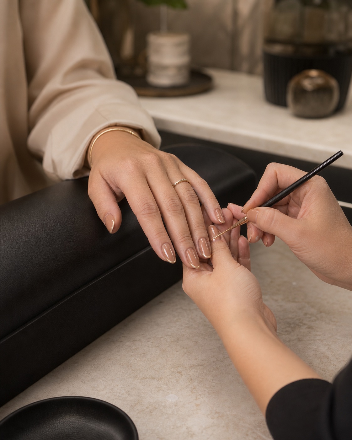 Manicure aplicando detalhe dourado em unhas de tom nude